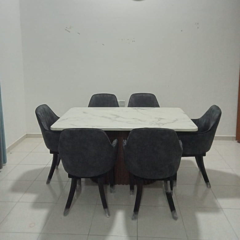A modern dining set featuring a rectangular white marble-patterned table surrounded by six dark gray upholstered chairs, set against a plain white wall with a round wall clock.