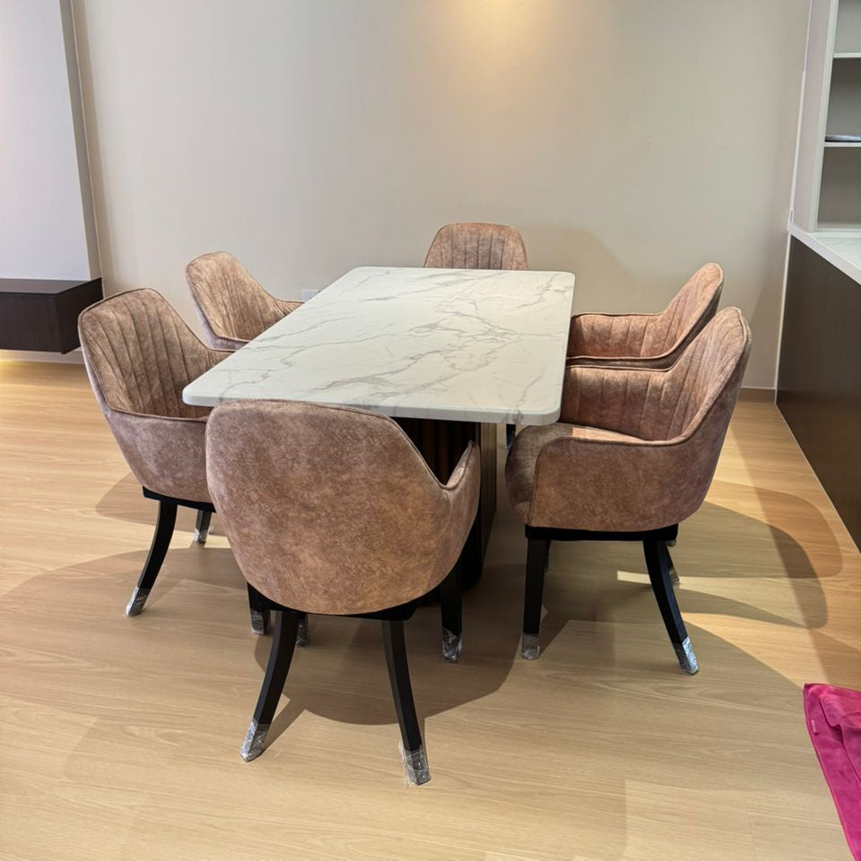 Dining area with a marble table and brown chairs in a room with light-colored walls and wooden flooring.
