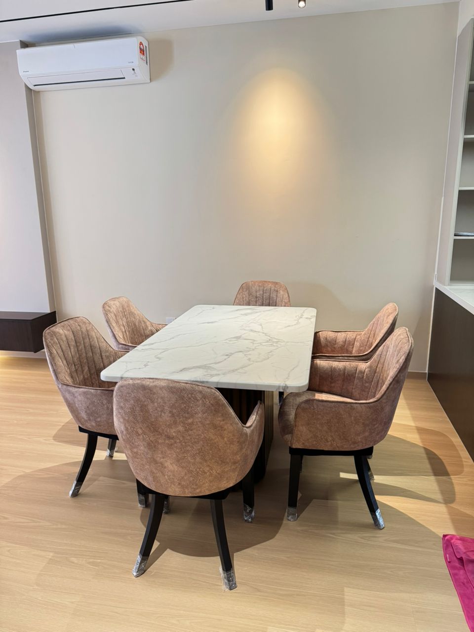 Dining area with a marble table and brown chairs in a room with light-colored walls and wooden flooring.