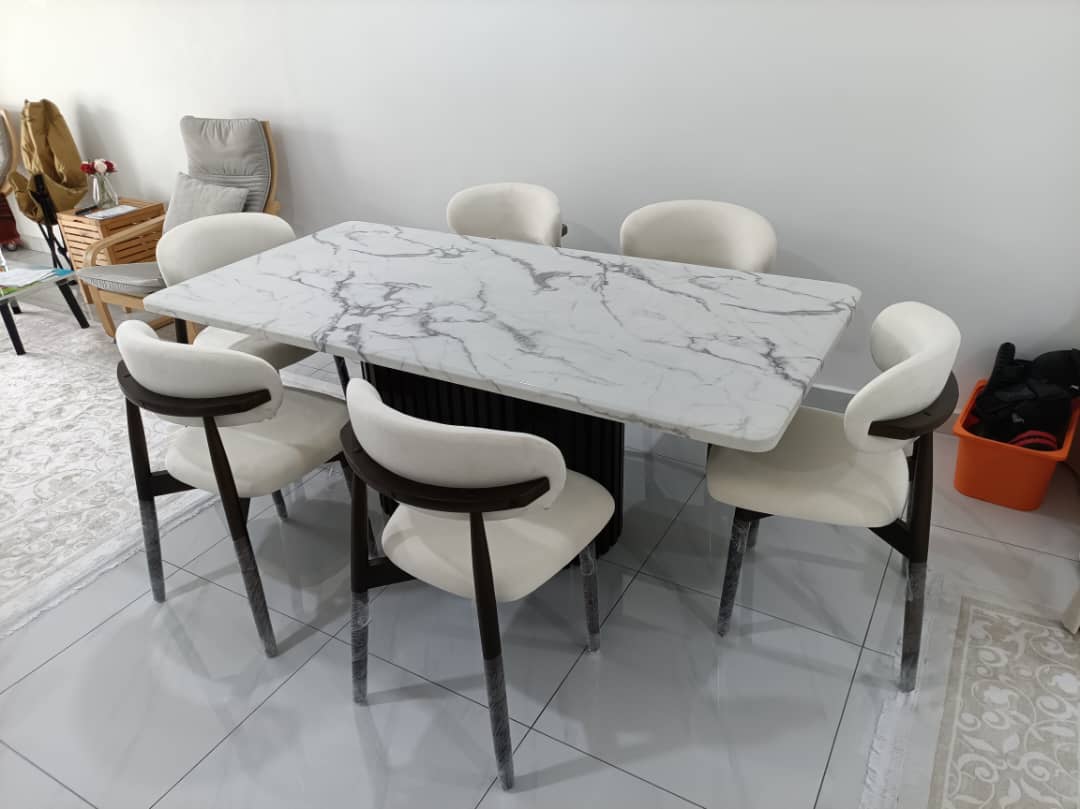 A modern 5-piece dining set featuring a rectangular white marble-patterned table and six matching chairs with cream upholstery and dark wood accents, shown in a home interior setting.