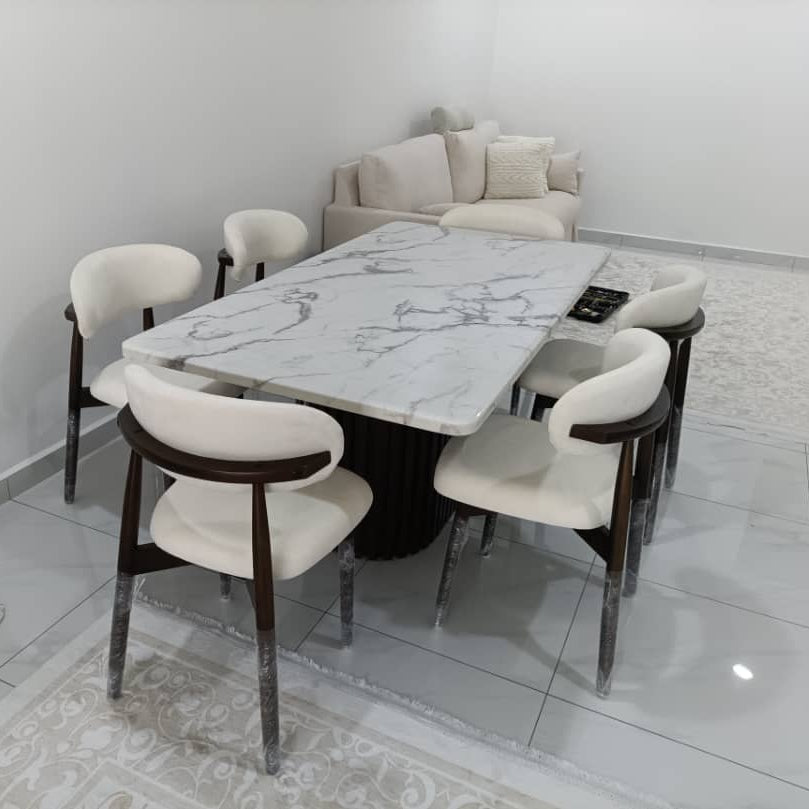 A modern dining set featuring a rectangular white marble-patterned table with a black pedestal base, surrounded by six white upholstered chairs with dark wood armrests and chrome legs, set in a minimalist dining room.